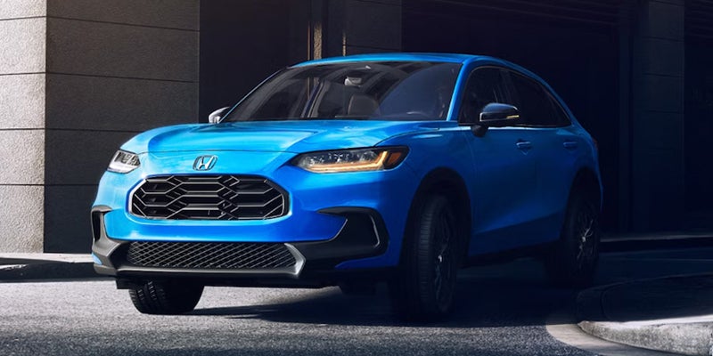 A bright blue Honda HR-V SUV parked angled left on a gray pavement, with a dark building in the background.