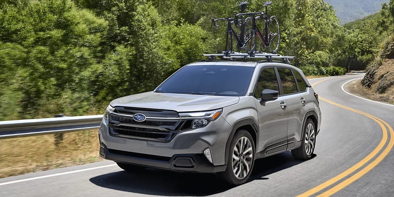 2026 Subaru Forester driving on a winding road with roof bike rack