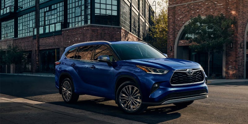 A dark blue SUV parked on a city street in front of brick industrial buildings.
