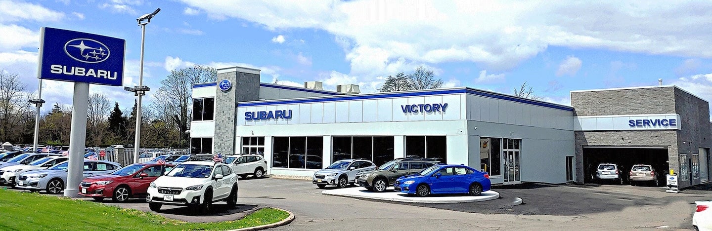 An exterior view of a Subaru Victory dealership with multiple new cars parked outside under a blue sky.