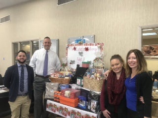 Four people stand behind a table laden with gift baskets and donations for The Little Ones.