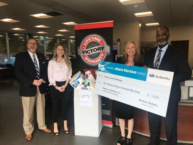 Four people holding a large check for $2,753 from Subaru and a box of donated household items.