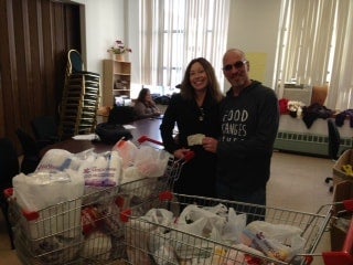 Two people standing proudly next to shopping carts overflowing with donated groceries, likely for a food drive.