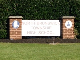 Red brick sign for North Brunswick Township High School with white lettering, flanked by school emblems.