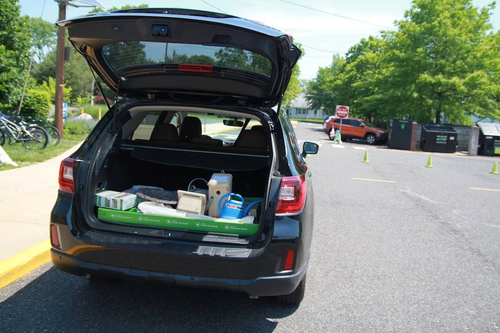 A black SUV with its trunk open, revealing gardening supplies in a green tray.