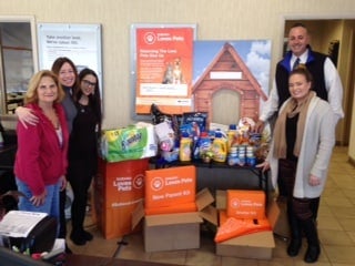 Five people stand around pet food and supplies collected for Subaru Loves Pets campaign.