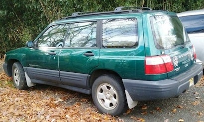 A dark green Subaru Forester SUV parked on brown leaves, seen from the right rear side.