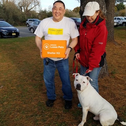 Man in Second Chance shirt holding a Subaru Loves Pets Shelter Kit box, with a woman and white dog with leash.