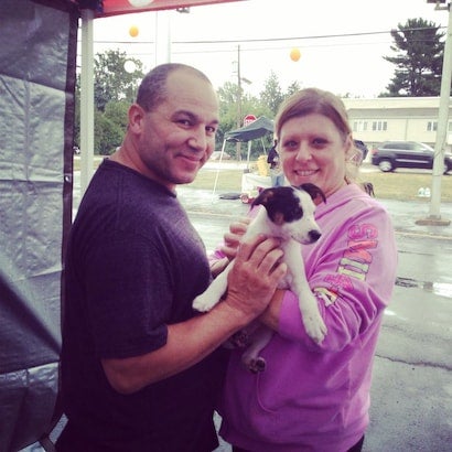 A man and woman smiling at the camera while holding a small black and white puppy.