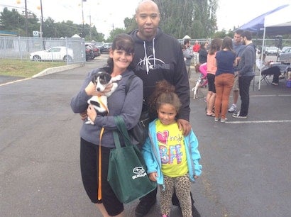 A family-of-three, including a small girl in leopard pants, and a woman holding a small puppy in a parking lot.
