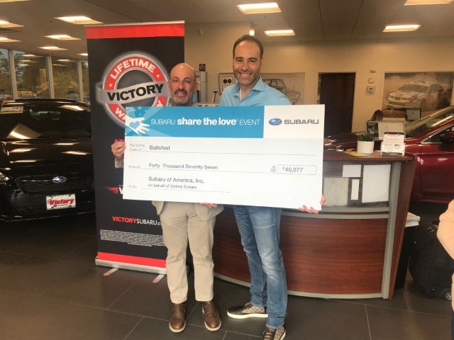 Two men holding an oversized check for $40,077 from Subaru of America, Inc. on behalf of Victory Subaru.