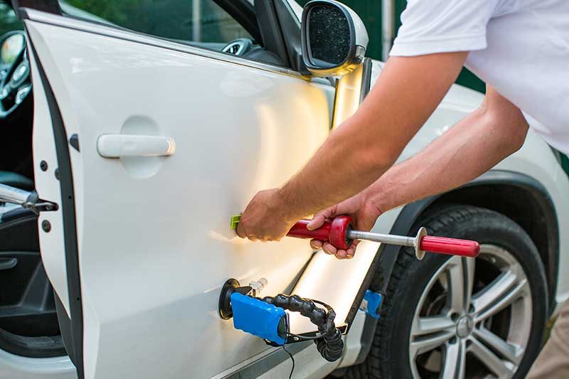 Technician using a specialized tool for paintless dent repair on a car