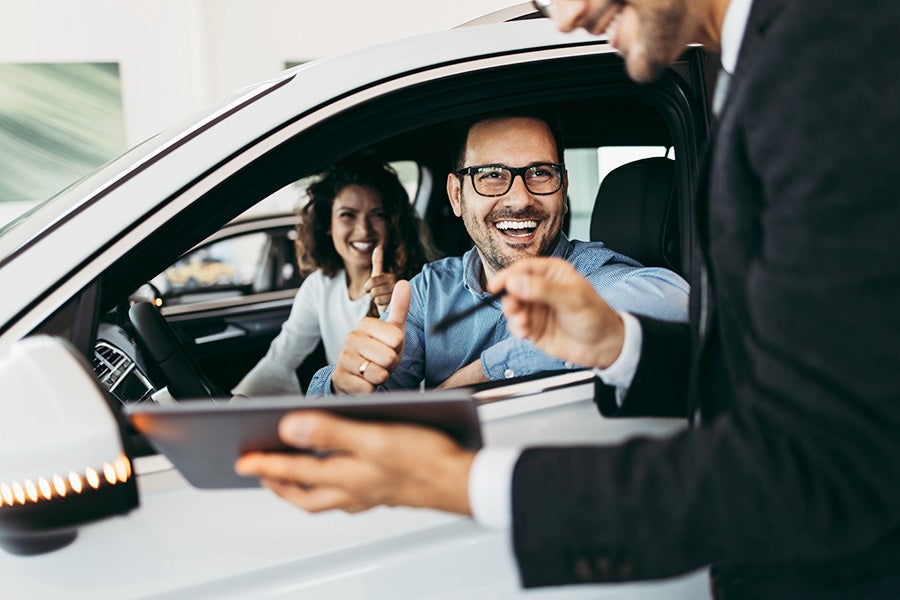 Happy couple giving thumbs up while sitting in a new white car