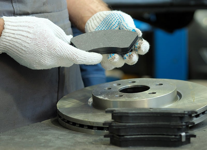 A person wearing white gloves holding a brake pad over a rotor
