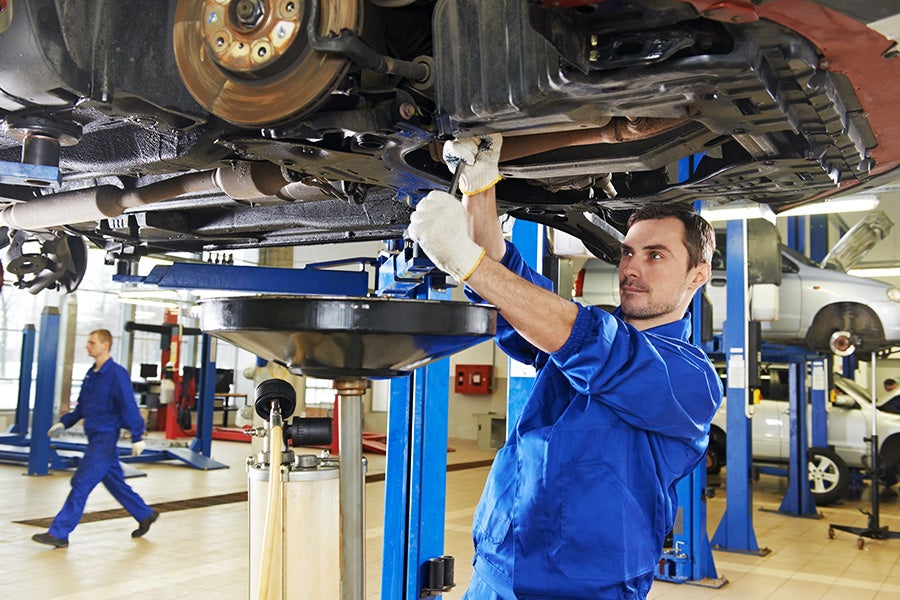 Mechanic in blue uniform working on the undercarriage of a lifted car