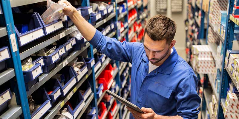 Worker in blue uniform checking car parts inventory using a digital tablet