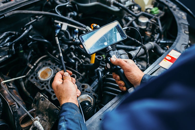 Mechanic using a digital borescope camera to inspect a car engine